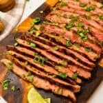 Garlic soy grilled flank steak sliced against the grain topped with cilantro, green onions, lime slices.