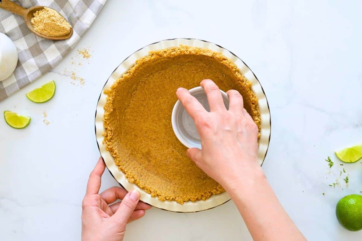 Easy Key Lime Pie with Homemade Graham Cracker Crust Cup pressing graham cracker crust into homemade pie plate.