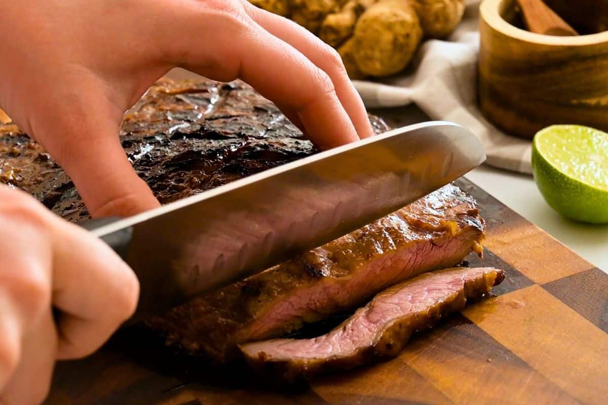 Grilled Flank Steak Recipe Chef's knife slicing the grilled flank steak against the grain.