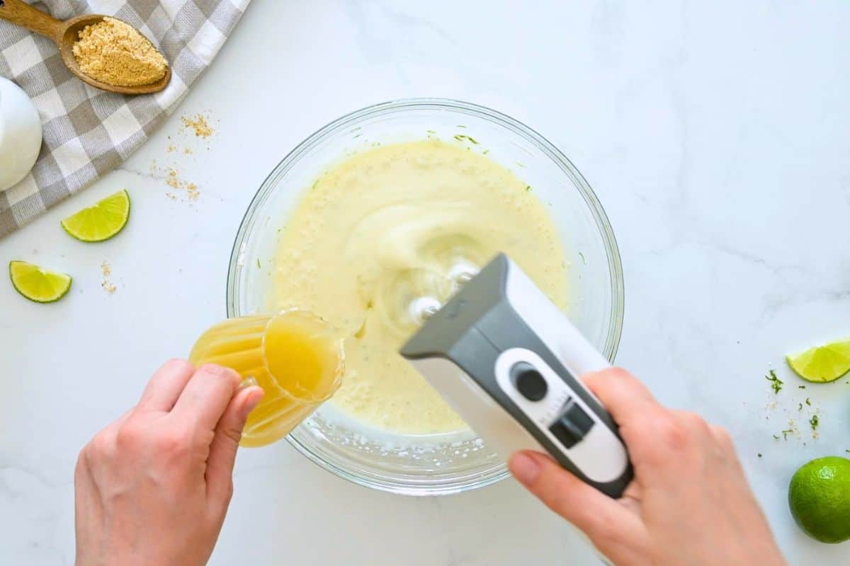 Key Lime Pie Recipe with Fresh Whipped Cream Handheld mixer mixing key lime pie filling while key lime juice is being slowly drizzled into mixing bowl.
