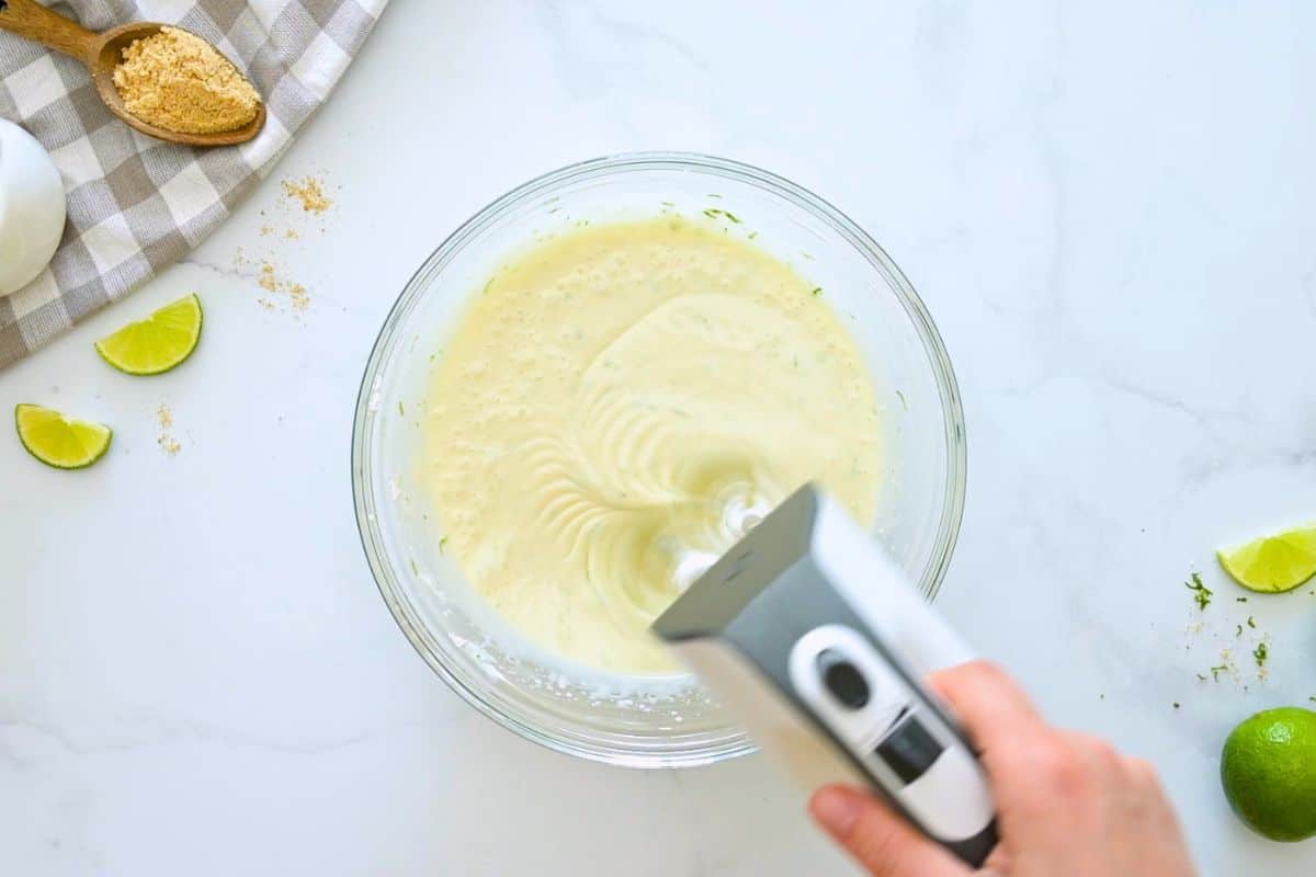 Recipe Key Lime Pie Handheld mixer mixing lime zest and sweetened condensed milk into cream cheese.