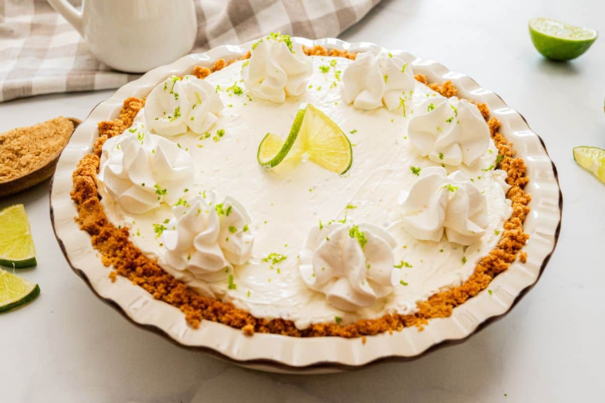 Easy Key Lime Pie Recipe Frozen Homemade key lime pie topped with fresh whipped cream, fresh lime slices, lime zest in homemade graham cracker crust.