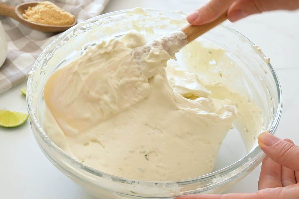 key lime pie recipe no eggs Fresh whipped cream being slowly folded into key lime cream cheese mixture using a spatula to lift up and over.