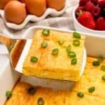 Slice of baked cottage cheese egg being lifted by spatula from casserole dish showing fluffy eggs with a few small curds of cottage cheese.