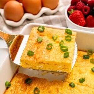 Slice of baked cottage cheese egg being lifted by spatula from casserole dish showing fluffy eggs with a few small curds of cottage cheese.