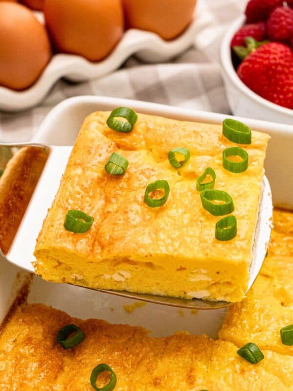 Slice of baked cottage cheese egg being lifted by spatula from casserole dish showing fluffy eggs with a few small curds of cottage cheese.