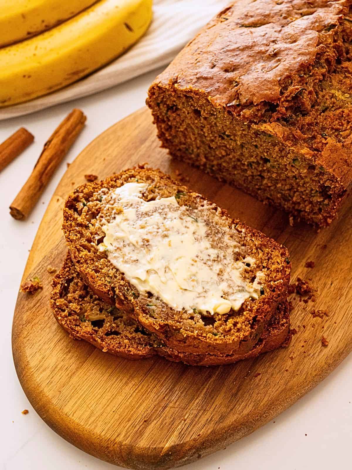 A slice of Zucchini banana bread on cutting board with generous smear of softened butter.