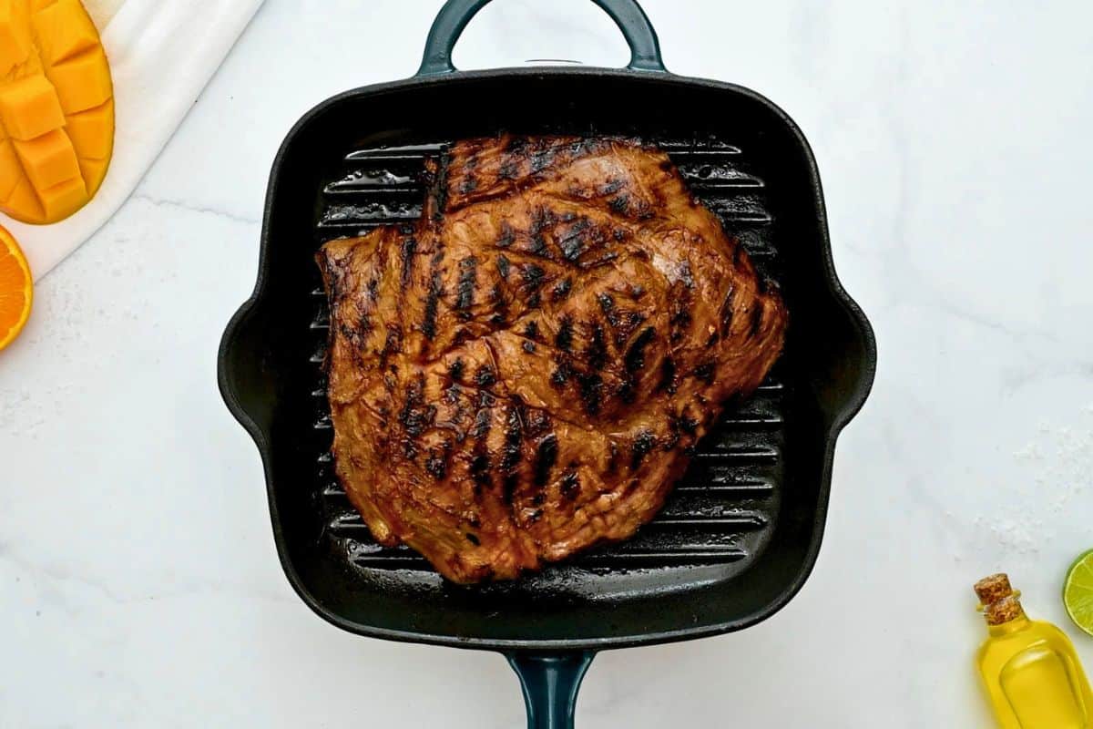 Grilled marinated flank steak on grill pan with scoring marks.