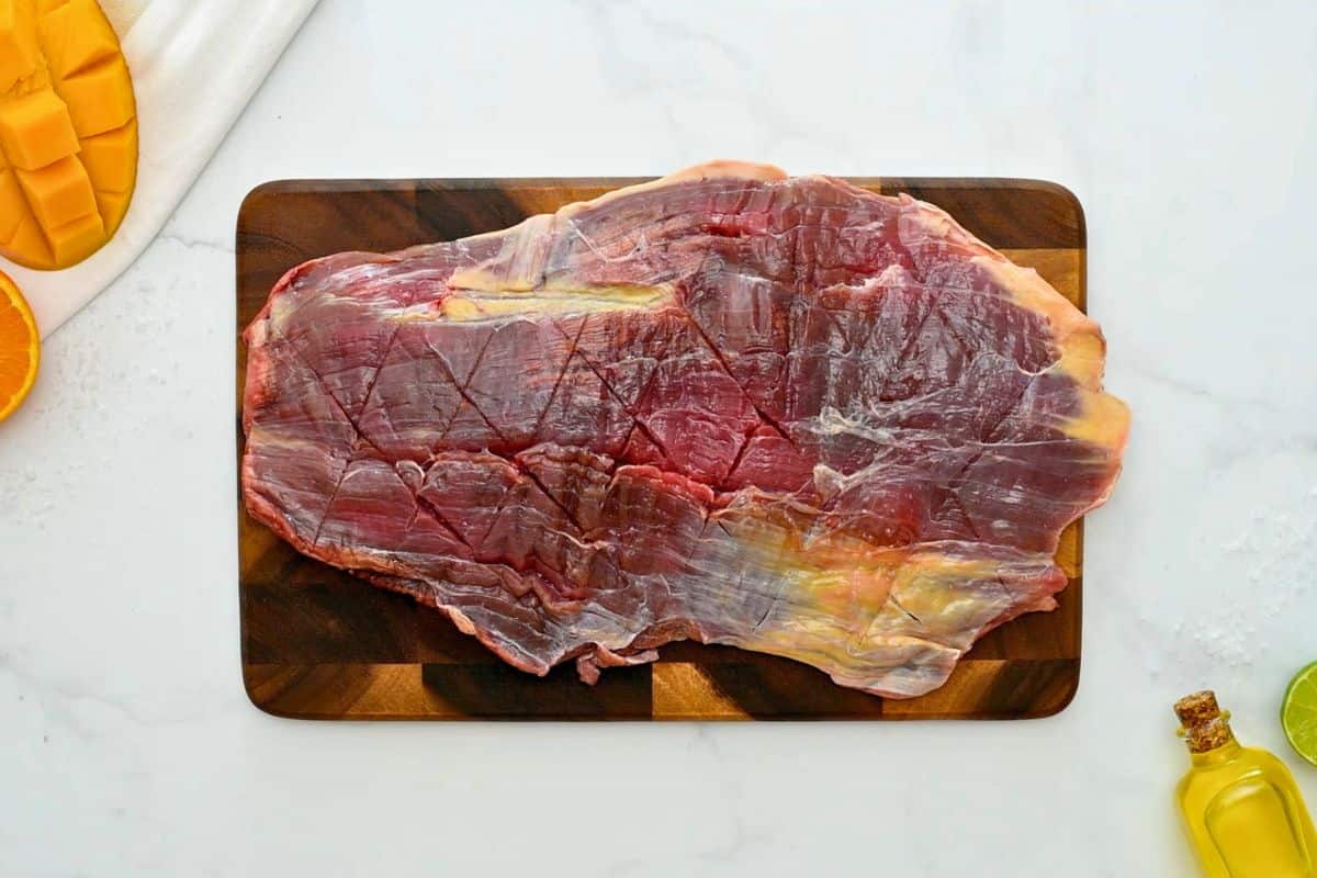 Flank steak on wooden cutting board lightly scored in diamond pattern.