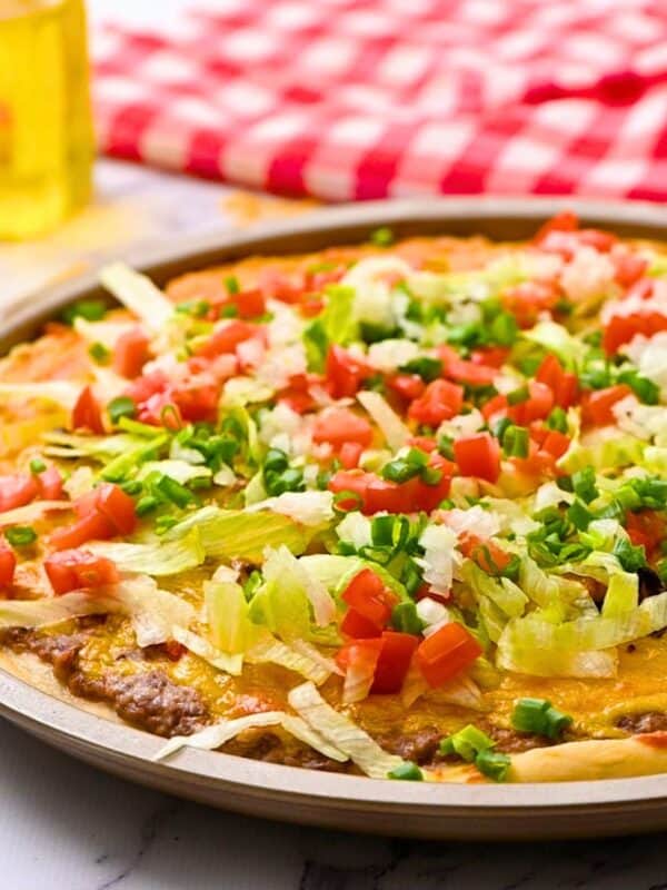 Baked pizza with refried beans, salsa, taco meat, cheese layered on pizza dough topped with shredded lettuce and diced tomatoes.