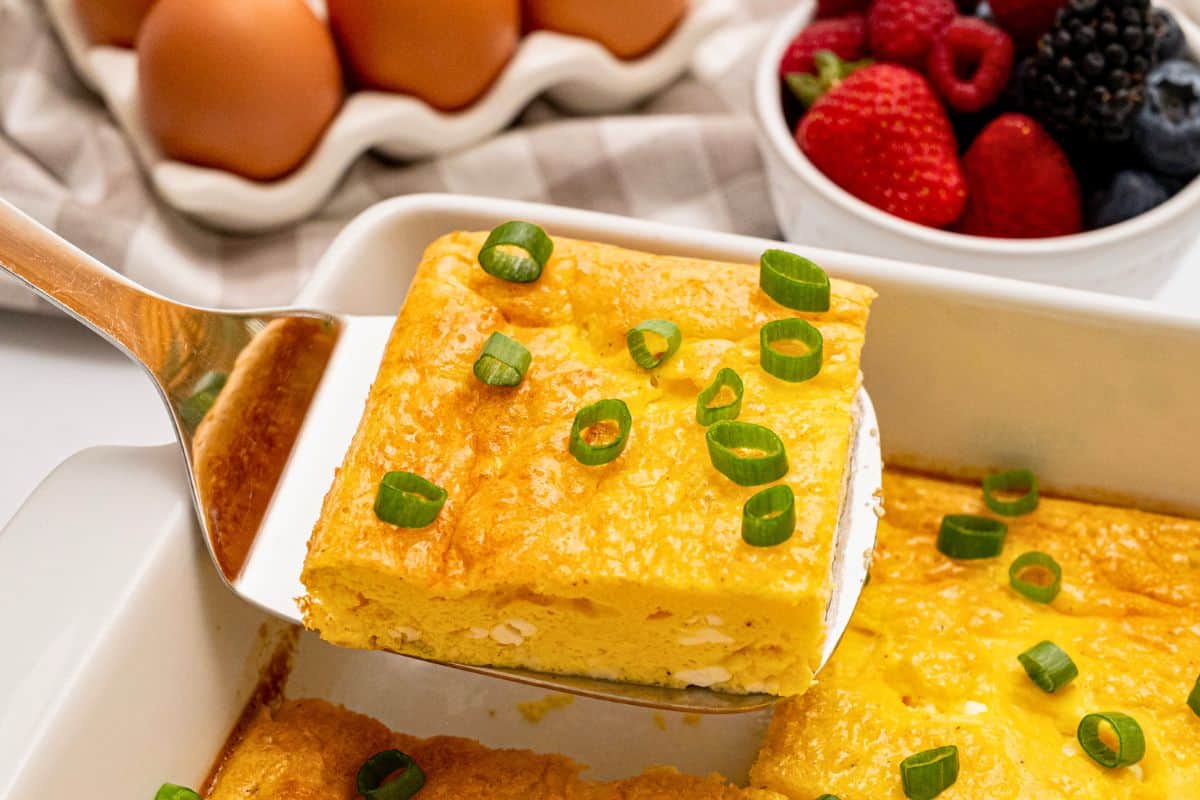 Easy Egg and Cottage Cheese Bake Slice of baked cottage cheese egg being lifted by spatula from casserole dish showing fluffy eggs with a few small curds of cottage cheese.