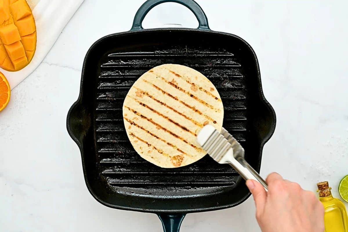 Flour tortilla being removed from grill plate after lightly toasting on each side.