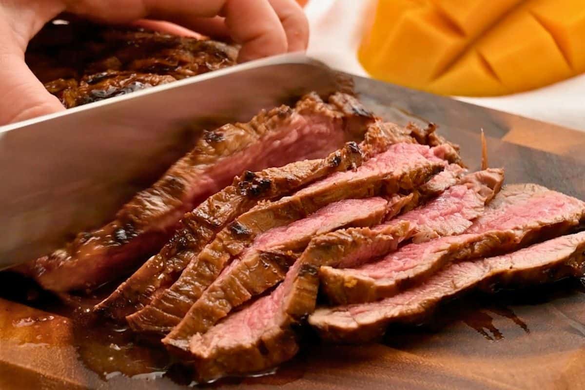 Knife cutting perpendicular to the fibers of the meat across marinated and grilled flank steak.