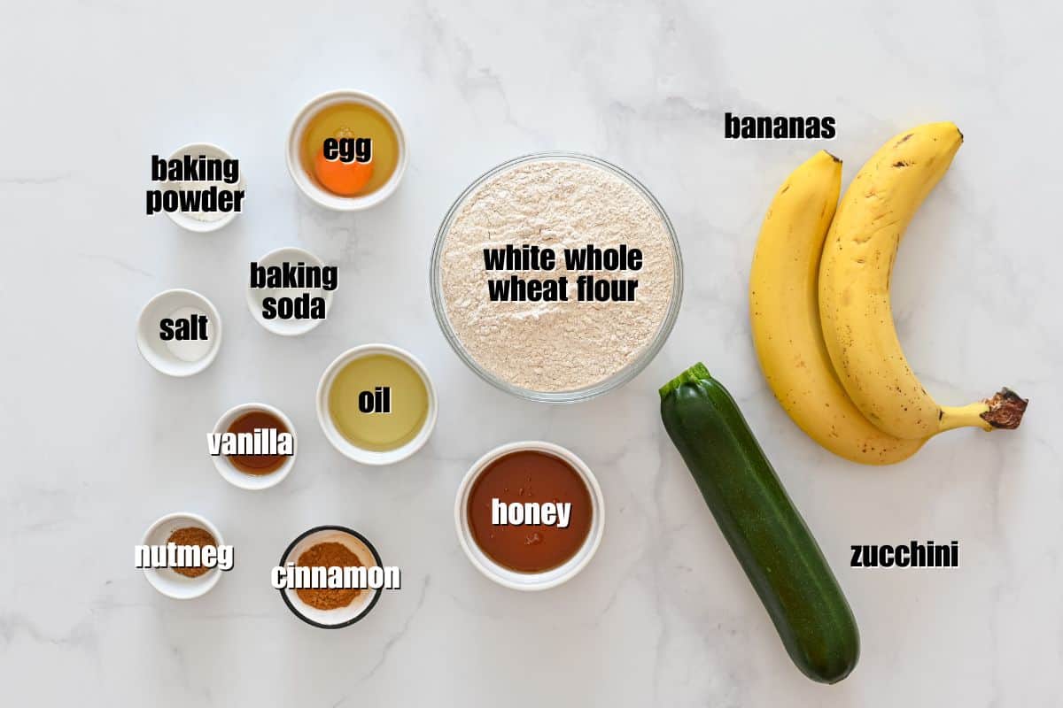 Recipe for Zucchini Banana Bread 2 ripe bananas, 1 small zucchini, whole wheat flour, honey, oil,, egg, and spices laid out on counter.