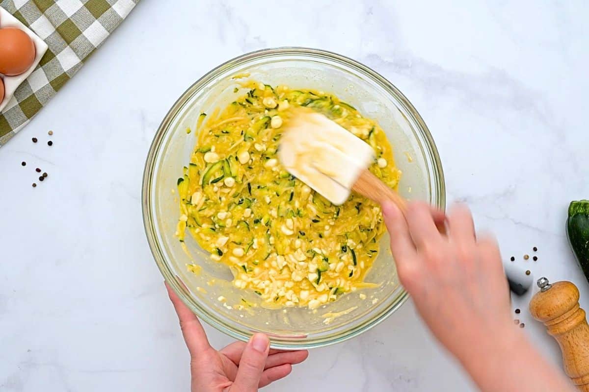 Savory Zucchini Pie with Eggs Spatula folding grated zucchini and onion into egg and cottage cheese mixture.