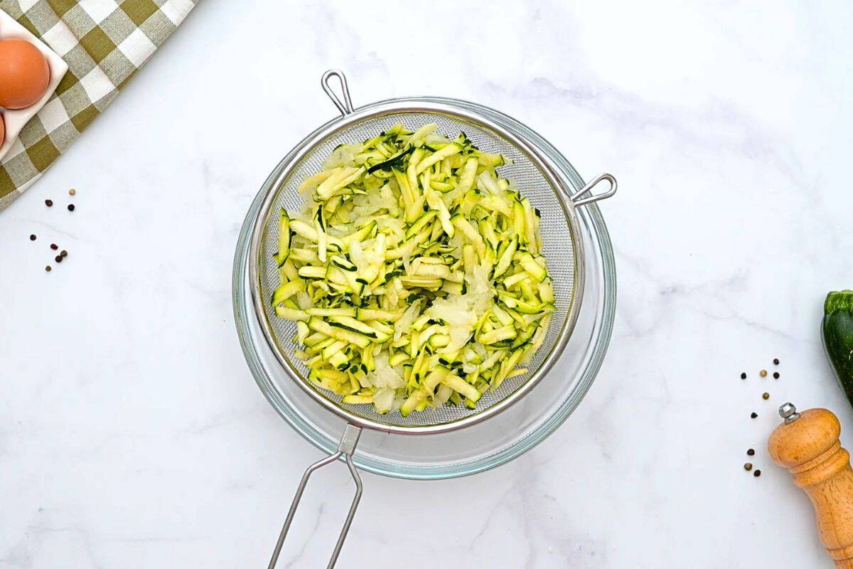 Shredded Zucchini Pie Salted shredded zucchini and grated onion in a fine-mesh strainer over large mixing bowl.