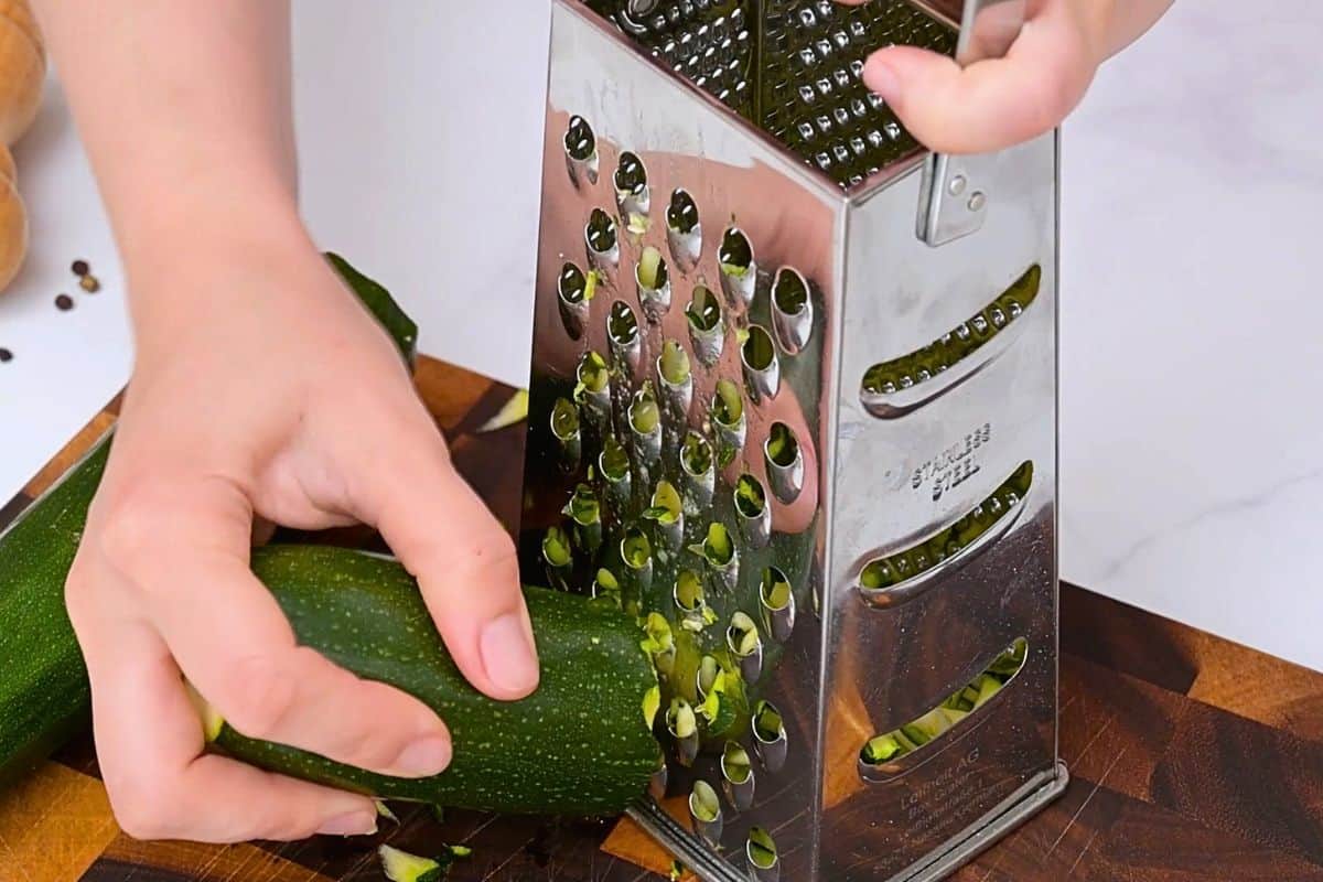 Shredded Zucchini Pie Zucchini being coarsely grated on box grater.