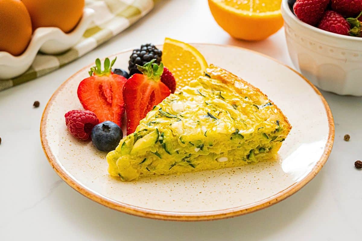 Zucchini Egg Pie Slice of crustless zucchini pie showing shredded zucchini and cottage cheese in pie next to fresh fruit.