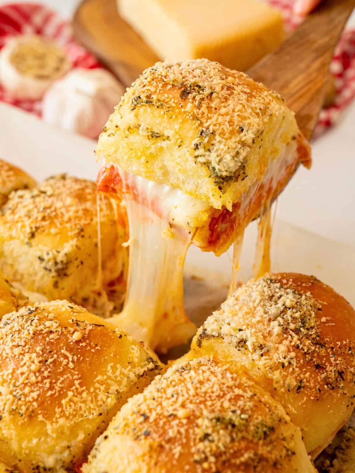 Baked slider made with pizza toppings and garlic butter being picked up showing a melted cheese pull.