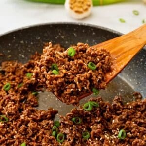 Wooden spoon scooping up ground beef with thick and glossy Korean-style stir-fry sauce.
