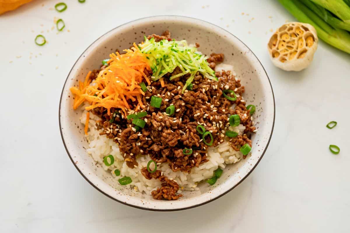Ground beef with gochujang sauce served over fluffy white rice and topped with grated carrots and cucumbers and sliced green onions.