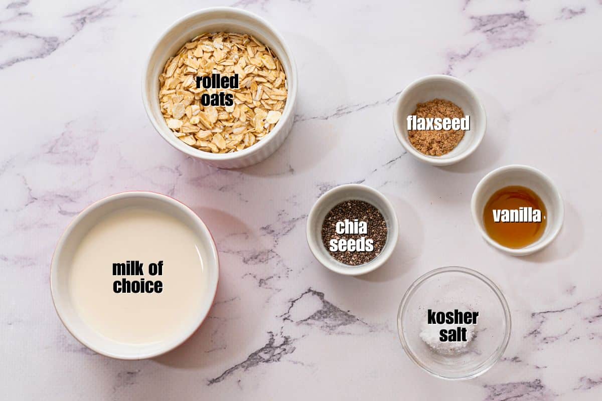 Overnight Oat Base Recipe Oats, milk, salt, chia, vanilla extract and flaxseed measured out in small bowls for one serving of overnight oats.