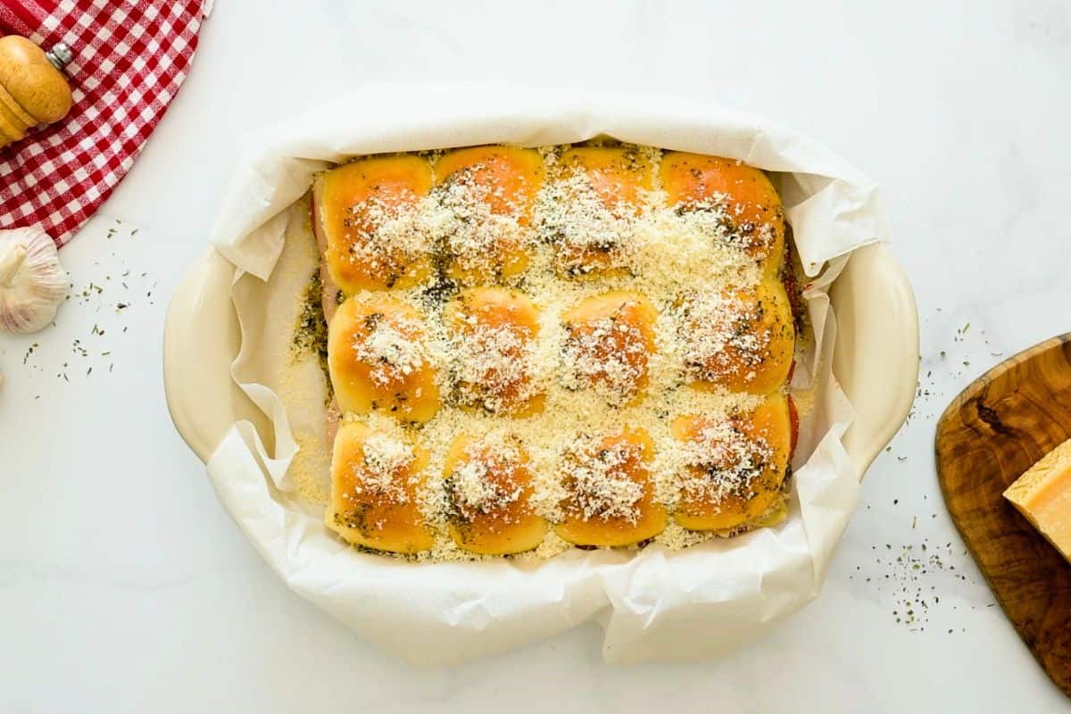 Partially baked pizza sliders in baking dish topped with grated parmesan cheese.
