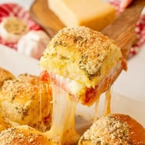 Baked slider made with pizza toppings and garlic butter being pulled away from rest of the sliders, showing a melted cheese pull.
