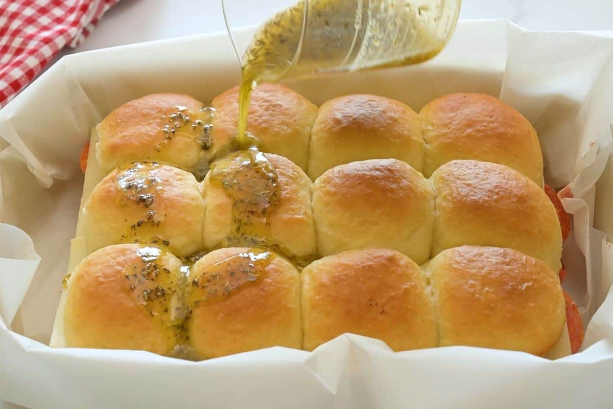 Garlic butter with Italian seasoning being slowly drizzled over assembled pizza sliders.