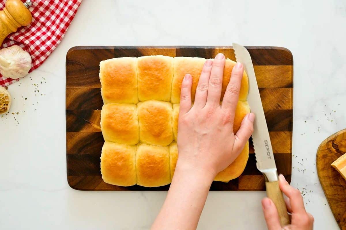 Serrated knife cutting Hawaiian rolls into half horizontally into bottom and top rolls.