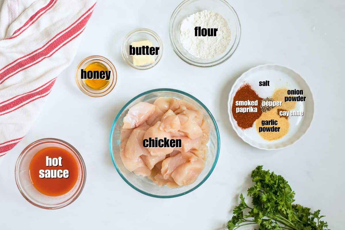 Easy Buffalo Chicken Bites Recipe Cubed chicken breast, flour, seasonings, butter, honey, and hot sauce labeled on counter to make buffalo chicken bites.