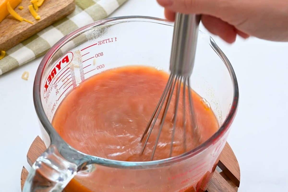 Buffalo Chicken Casserole with Rice Chicken stock being whisked with hot sauce and seasonings in large glass measuring cup.
