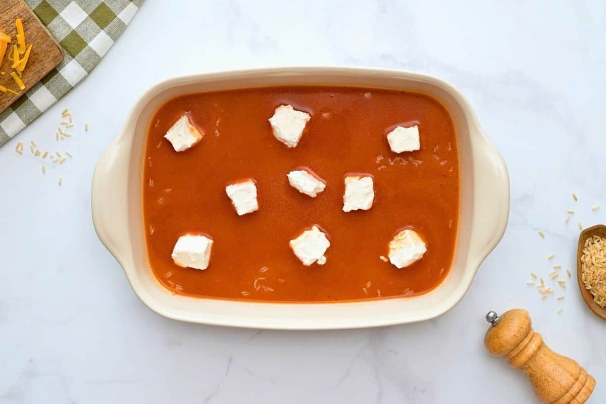 No Peek Buffalo Chicken and Rice Buffalo sauce mixture, uncooked brown rice, and cubed cream cheese layered in casserole dish.
