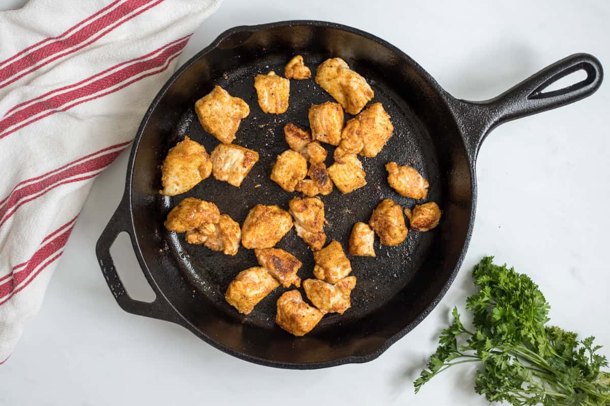 Buffalo Chicken Recipe Bite Sized Browned chicken bites that have been tossed with seasoned flour in cast iron skillet.