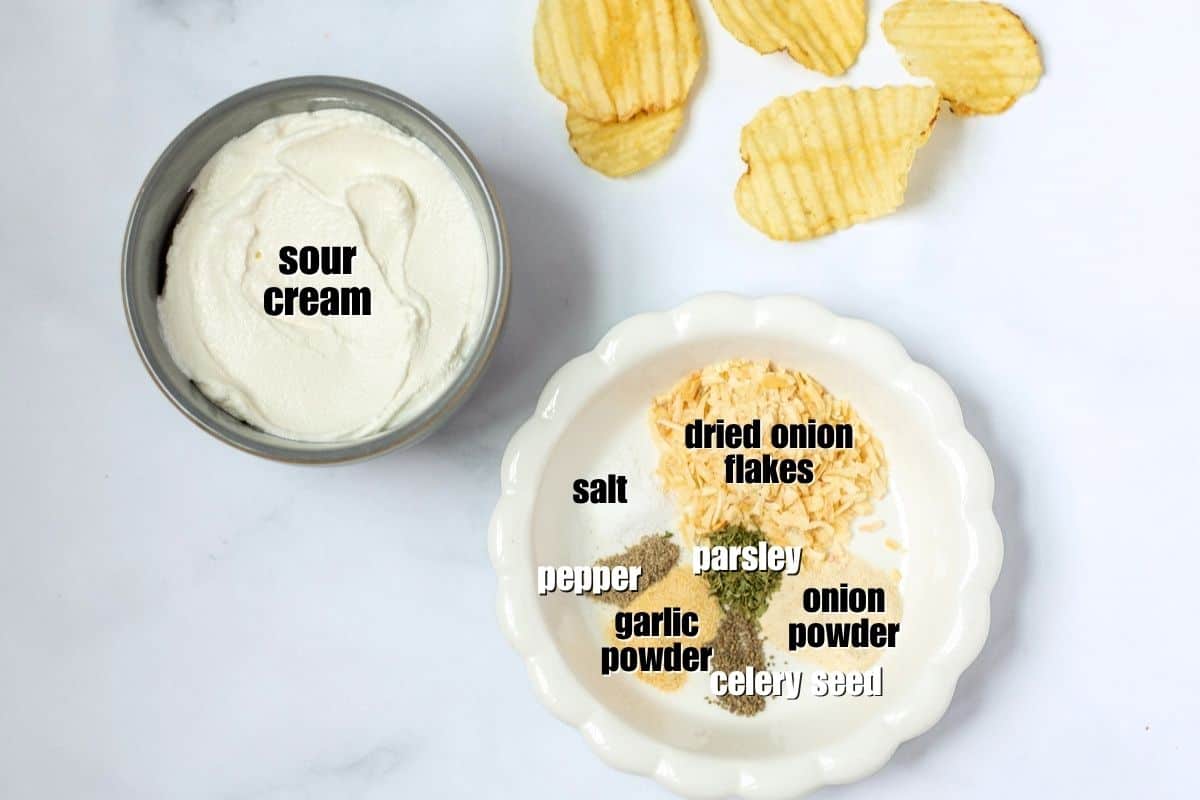 The Best Chip Dip Recipe Sour Cream, dried onion flakes, onion powder, garlic powder, salt, pepper, celery seed, parsley and ridged potato chips on counter.