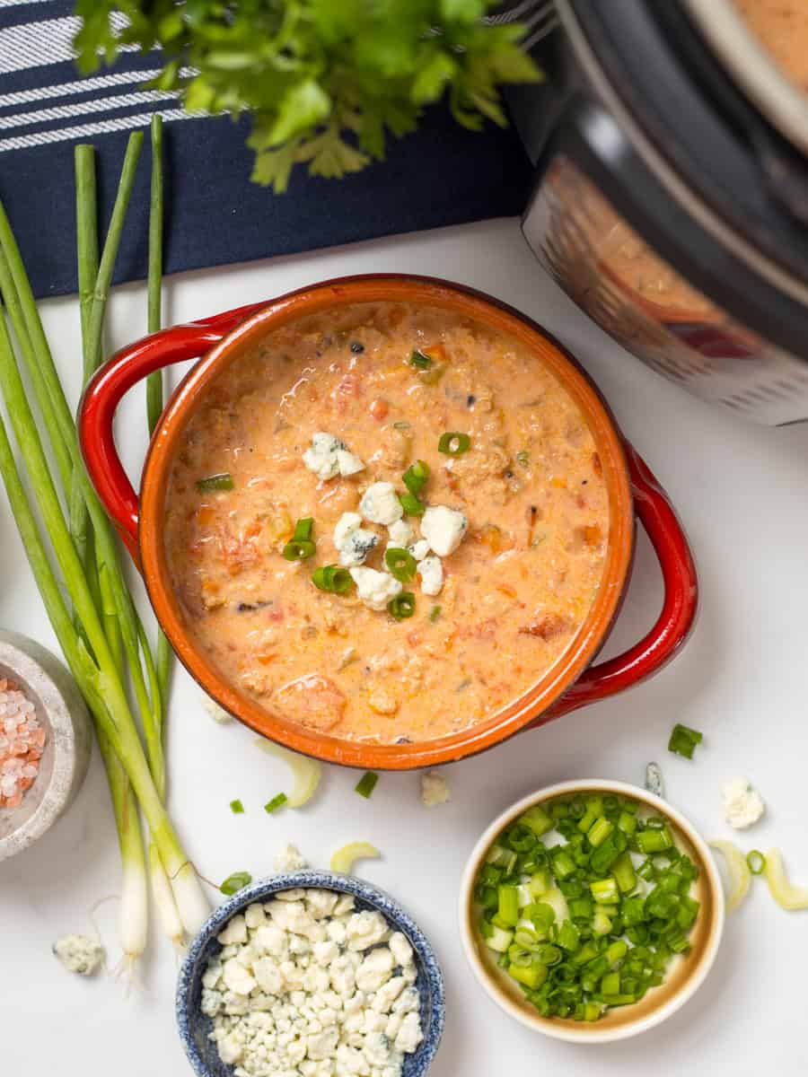 Instant Pot Buffalo Chicken Chili Bowl of creamy Buffalo Chicken Chili topped with crumbled blue cheese and sliced green onions next to Instant Pot.