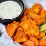 Crispy breaded boneless wings brushed with buffalo sauce piled in basket with side of ranch, celery, and carrots.