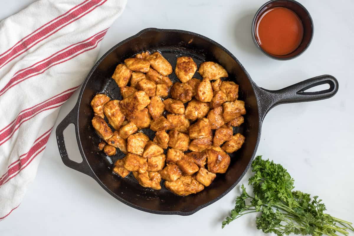 Chicken Bites with Buffalo Sauce Cast iron skillet with browned seasoned chicken bites tossed in buffalo sauce.