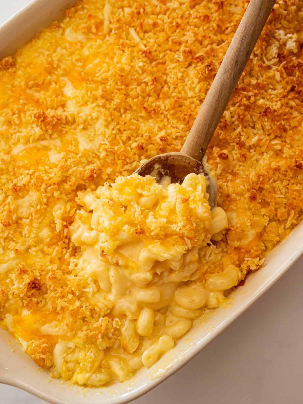 Wooden spoon scooping out creamy baked mac and cheese from a 9x13-inch baking dish.