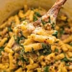 Spoonful of cooked pasta with Italian sausage and spinach in creamy sauce.
