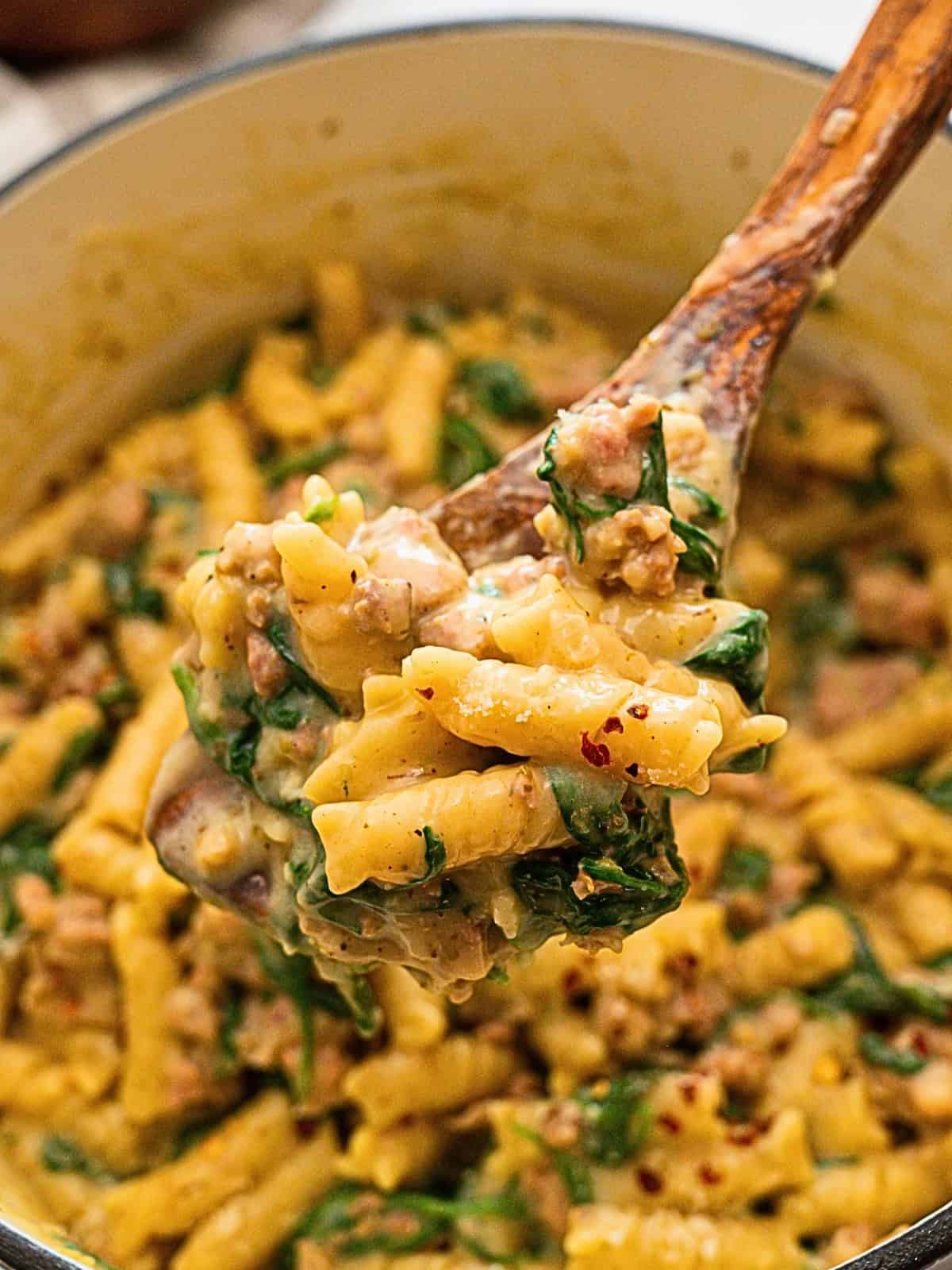 Spoonful of cooked rotini noodles with Italian sausage and spinach in creamy sauce.