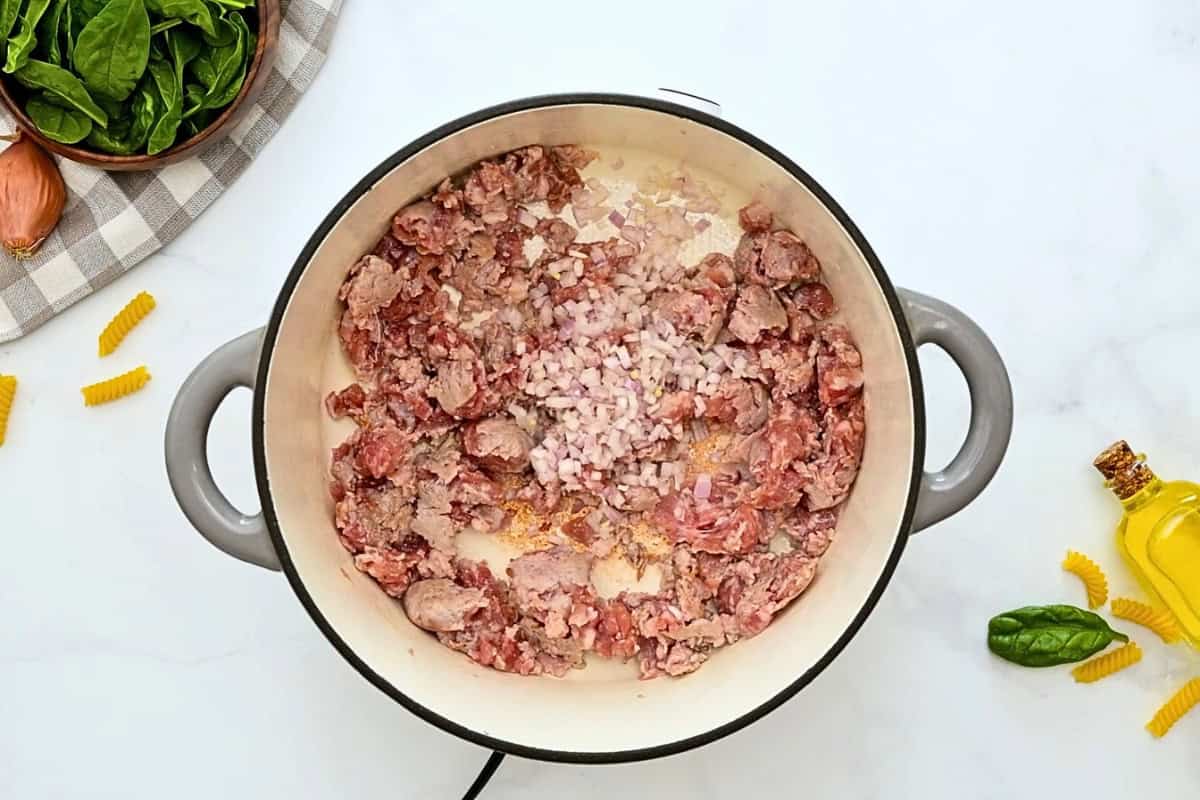 Partially browned Italian sausage with minced shallots in a large stockpot.