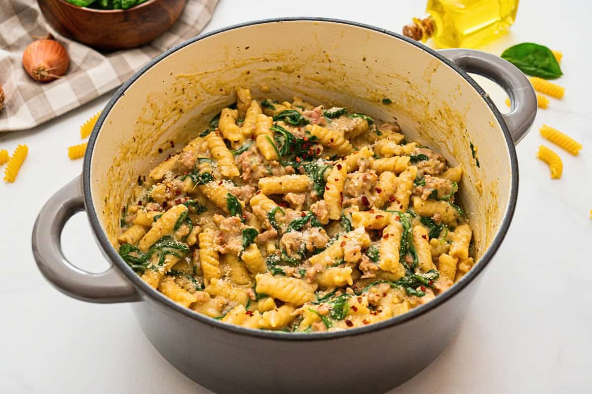 Stockpot with cooked rotini and Italian sausage in creamy sauce with wilted spinach.